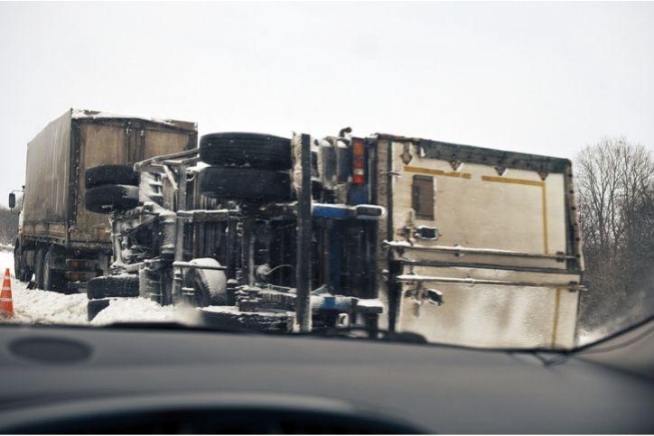 Truck accident on a snow-covered road. One truck is overturned and in the median